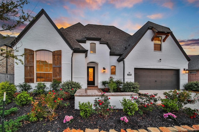 french country home with brick siding and a shingled roof
