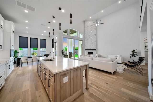 kitchen featuring visible vents, open floor plan, a high ceiling, a sink, and light wood-style flooring