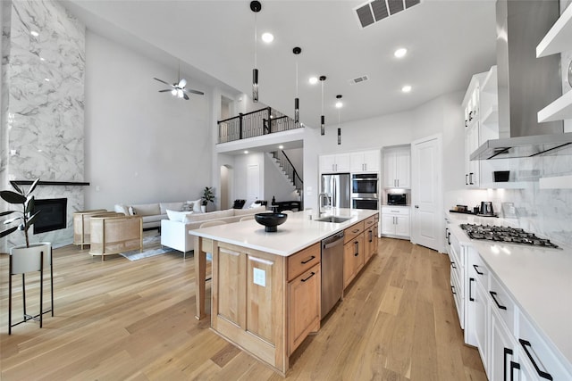 kitchen with wall chimney range hood, a high ceiling, appliances with stainless steel finishes, and visible vents