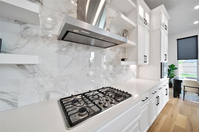 kitchen with open shelves, wall chimney range hood, light countertops, tasteful backsplash, and stainless steel gas stovetop