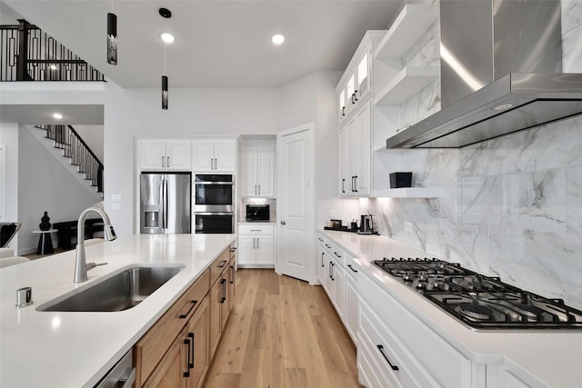 kitchen featuring wall chimney range hood, open shelves, stainless steel appliances, and a sink