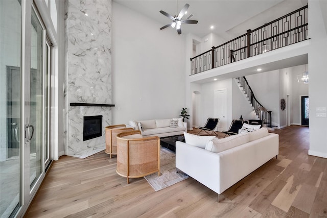 living area with ceiling fan, wood finished floors, stairway, a high ceiling, and a premium fireplace