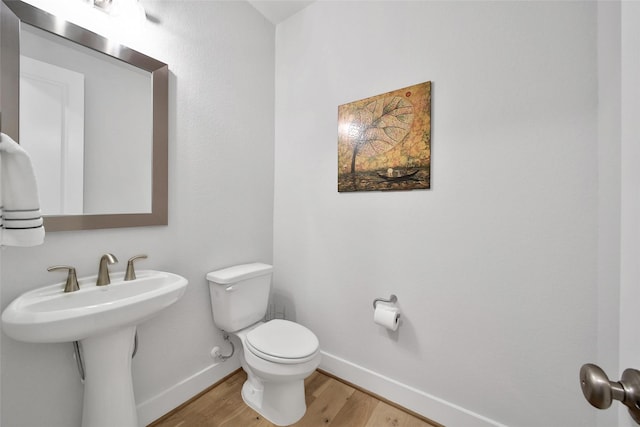 half bath with baseboards, wood finished floors, and toilet