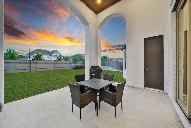 patio terrace at dusk with a lawn, a fenced backyard, and outdoor dining space
