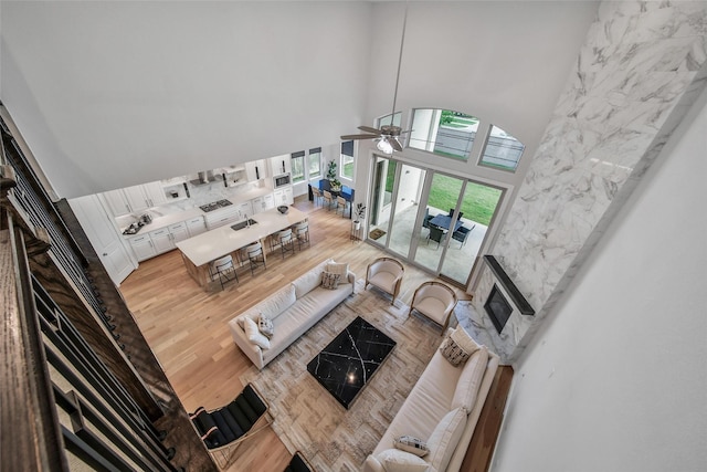 living area with a high ceiling, ceiling fan, and light wood-style flooring