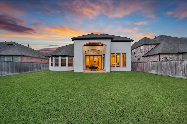 back of house at dusk featuring a lawn, stucco siding, a fenced backyard, and a patio area