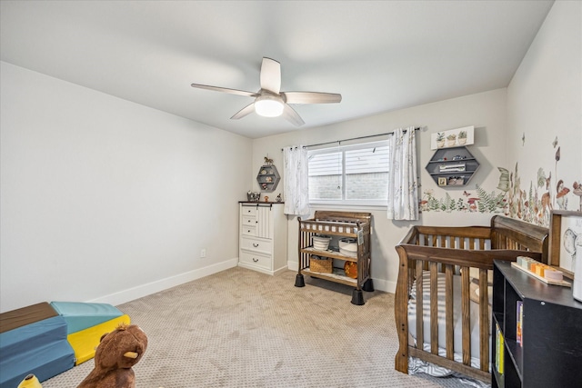carpeted bedroom with a crib, a ceiling fan, and baseboards