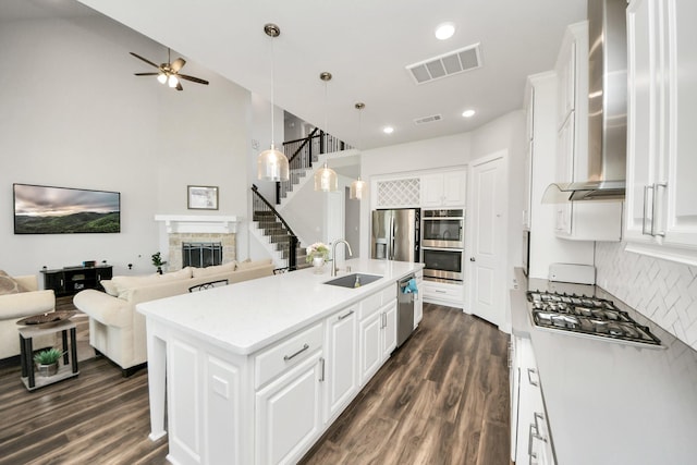 kitchen featuring wall chimney exhaust hood, a sink, open floor plan, visible vents, and appliances with stainless steel finishes