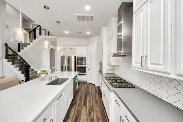 kitchen featuring wall chimney exhaust hood, white cabinets, a sink, visible vents, and appliances with stainless steel finishes
