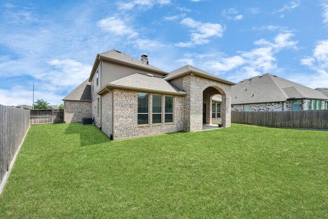 rear view of house featuring brick siding, a yard, a chimney, and a fenced backyard