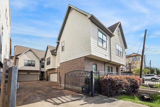 view of home's exterior featuring fence private yard, brick siding, a gate, an attached garage, and driveway
