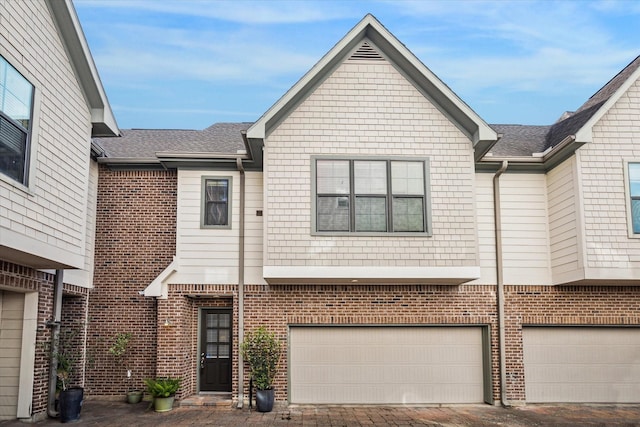 townhome / multi-family property with roof with shingles, an attached garage, driveway, and brick siding