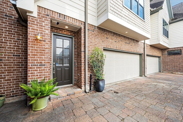 property entrance featuring a garage, decorative driveway, and brick siding