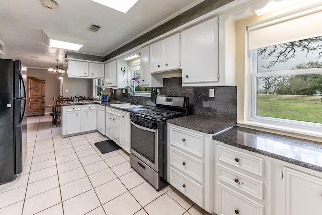 kitchen with a sink, light tile patterned floors, white cabinets, stainless steel range with gas stovetop, and freestanding refrigerator