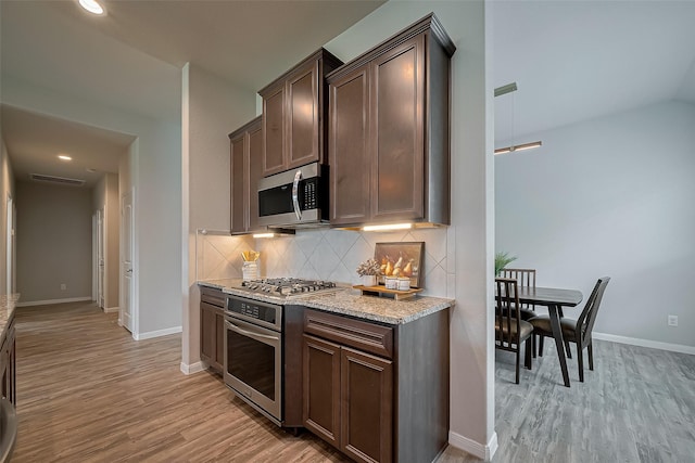 kitchen with light wood finished floors, baseboards, decorative backsplash, light stone counters, and appliances with stainless steel finishes