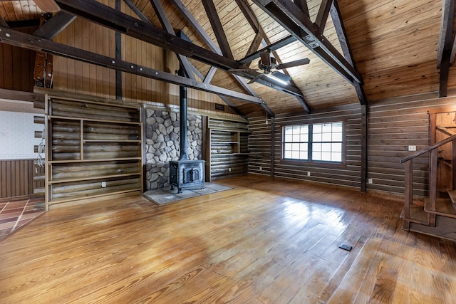 unfurnished living room featuring a wood stove, hardwood / wood-style flooring, stairs, and beam ceiling