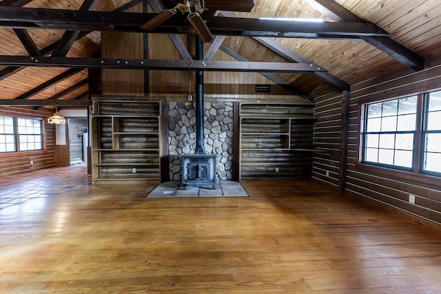 unfurnished living room with vaulted ceiling with beams, log walls, wood ceiling, hardwood / wood-style floors, and a wood stove