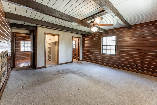 interior space with a walk in closet, multiple windows, carpet, wood walls, and beam ceiling