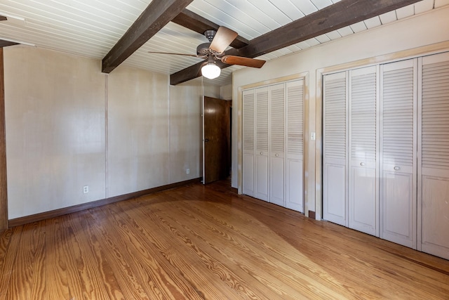 unfurnished bedroom with light wood-style floors, baseboards, multiple closets, and beam ceiling