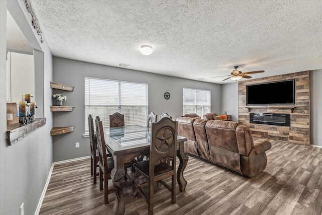 dining area featuring a large fireplace, a ceiling fan, baseboards, wood finished floors, and visible vents