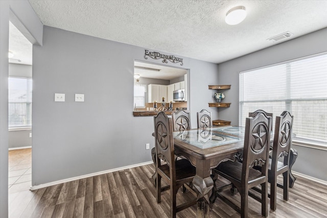 dining space with a textured ceiling, baseboards, wood finished floors, and visible vents