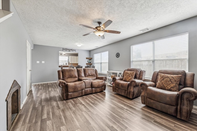 living area with a textured ceiling, a ceiling fan, baseboards, wood finished floors, and visible vents