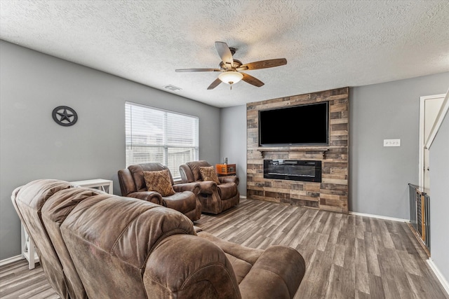 living area with visible vents, wood finished floors, baseboards, a stone fireplace, and ceiling fan