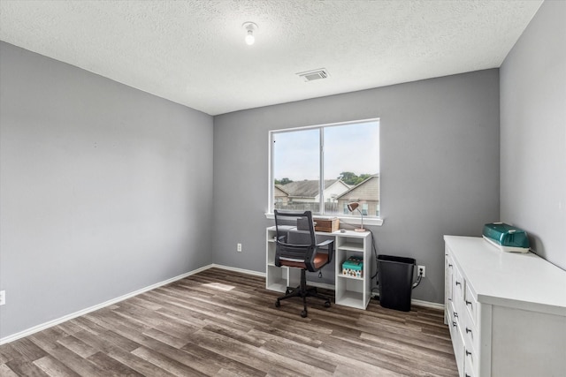 home office with a textured ceiling, baseboards, wood finished floors, and visible vents
