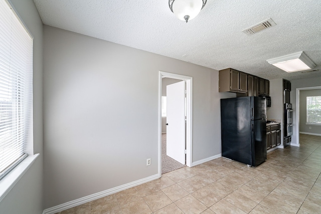kitchen featuring dark brown cabinetry, a textured ceiling, visible vents, light tile patterned floors, and freestanding refrigerator