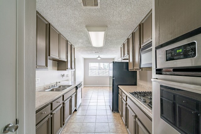 kitchen featuring light countertops, a textured ceiling, a sink, light tile patterned floors, and stainless steel appliances