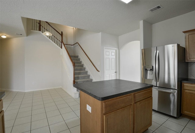 203 Annatto Ln, Crosby, TX 77532 - kitchen featuring stainless steel refrigerator with ice dispenser, dark countertops, light tile patterned floors, a kitchen island, and a textured ceiling