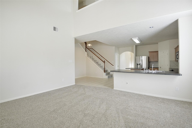 203 Annatto Ln, Crosby, TX 77532 - unfurnished living room featuring arched walkways, light carpet, stairway, baseboards, and a sink