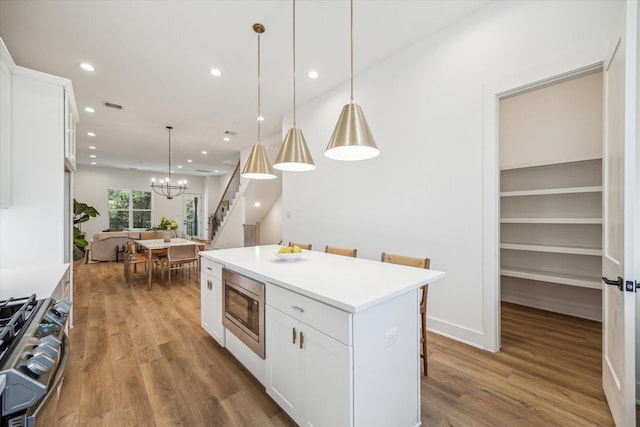 kitchen featuring white cabinets, a center island, light wood-type flooring, a notable chandelier, and appliances with stainless steel finishes