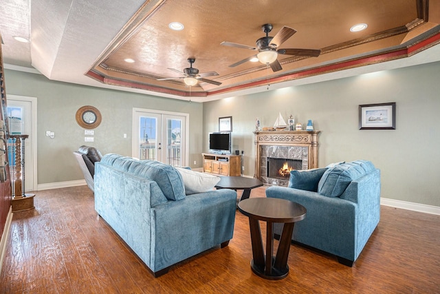 living room with ceiling fan, baseboards, wood finished floors, and a tray ceiling