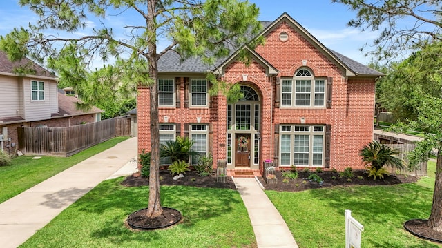 view of front of property featuring fence, roof with shingles, a front lawn, and brick siding