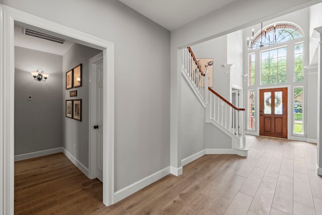 entrance foyer with an inviting chandelier, stairway, light wood-type flooring, visible vents, and baseboards