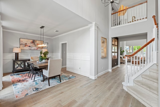 dining space with stairway, an inviting chandelier, ornamental molding, wood finished floors, and wainscoting