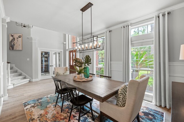 dining space featuring an inviting chandelier, stairs, light wood-style flooring, a decorative wall, and crown molding