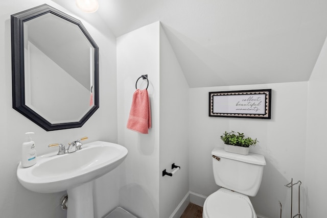 bathroom featuring baseboards, a sink, toilet, and vaulted ceiling