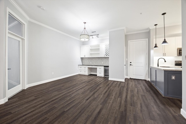 unfurnished living room featuring built in desk, dark wood finished floors, baseboards, and a sink