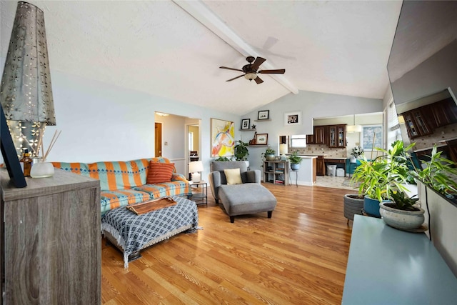 living room featuring ceiling fan, vaulted ceiling with beams, and light wood-style floors