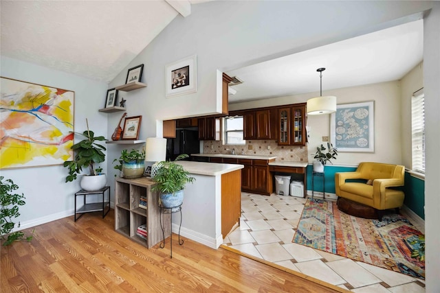 kitchen featuring black refrigerator, light countertops, glass insert cabinets, a peninsula, and tasteful backsplash