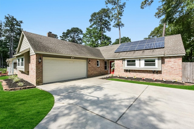 single story home featuring roof mounted solar panels, fence, concrete driveway, an attached garage, and brick siding