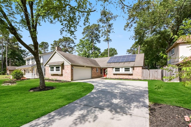 ranch-style home with an attached garage, a front lawn, roof mounted solar panels, and concrete driveway