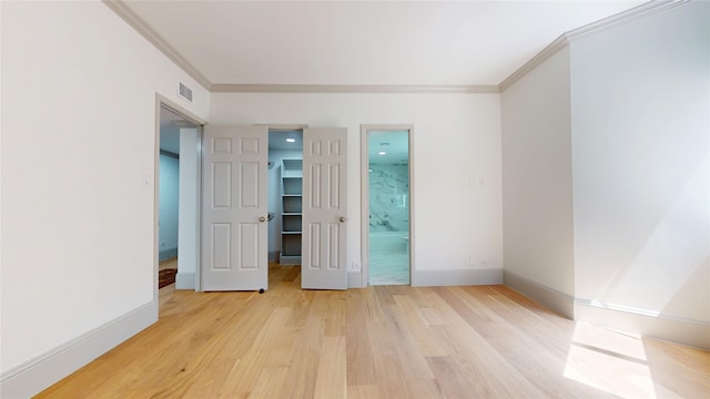 unfurnished bedroom featuring a spacious closet, visible vents, light wood-style floors, crown molding, and baseboards