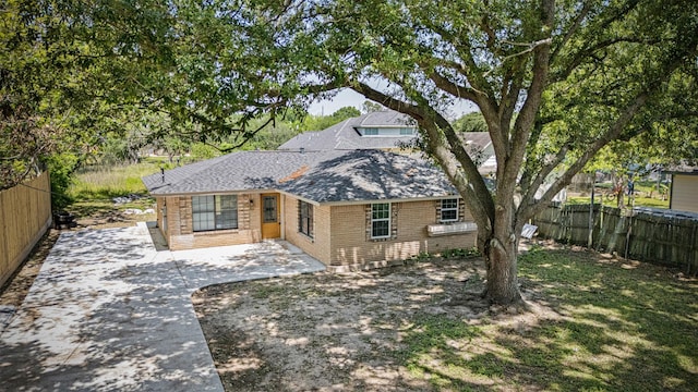 view of front facade with brick siding, a patio area, roof with shingles, and fence