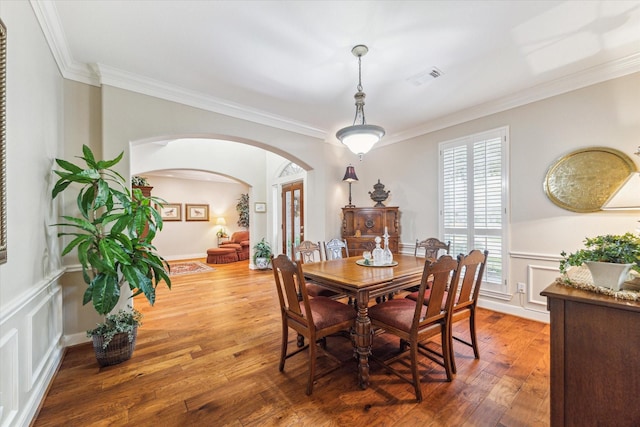 dining area featuring wood finished floors, visible vents, arched walkways, and ornamental molding