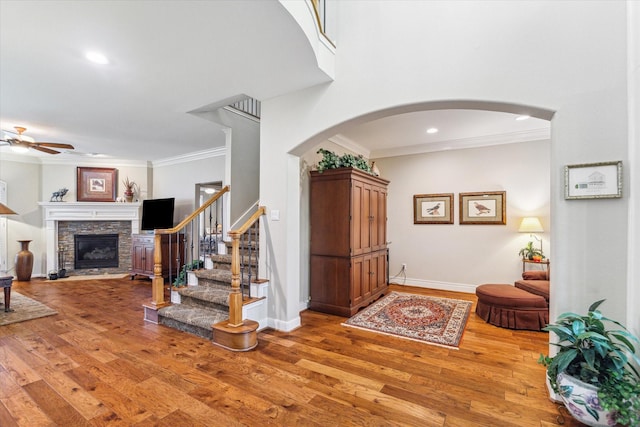 entryway featuring light wood-type flooring, a ceiling fan, stairway, crown molding, and a fireplace