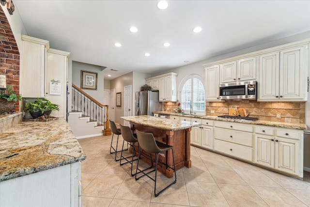 kitchen with tasteful backsplash, a kitchen bar, light stone counters, appliances with stainless steel finishes, and cream cabinets