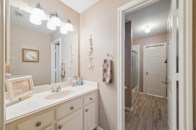 full bathroom featuring enclosed tub / shower combo, wood finished floors, visible vents, vanity, and baseboards